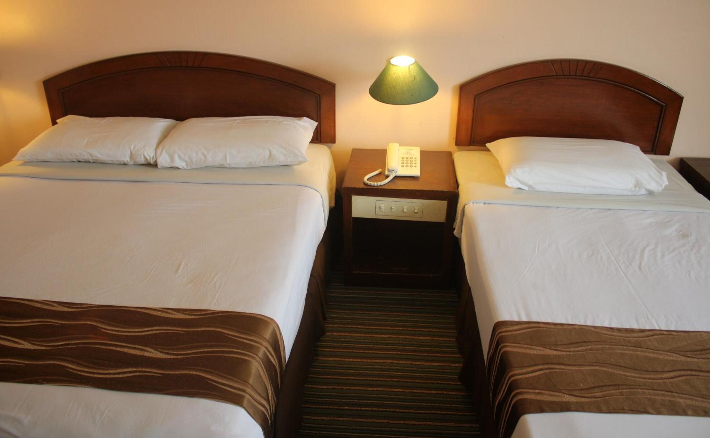 Une chambre d’hôtel avec deux lits, chacun doté d’une tête de lit en bois, d’une table de chevet avec une lampe et d’un téléphone.