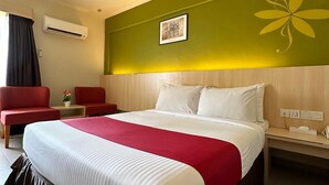 A hotel room with a large bed, a red and white bedspread, a wooden headboard, a red armchair, a small table with a vase of flowers, and an air conditioning unit on the wall. - Hotel Seri Malaysia Pulau Pinang (George Town)