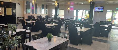 A spacious restaurant with multiple tables and chairs, star-shaped ceiling lights, and a television screen on the wall.