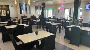 A modern restaurant with black chairs and tables, large windows, and decorative plants. - Hotel Seri Malaysia Pulau Pinang (George Town)