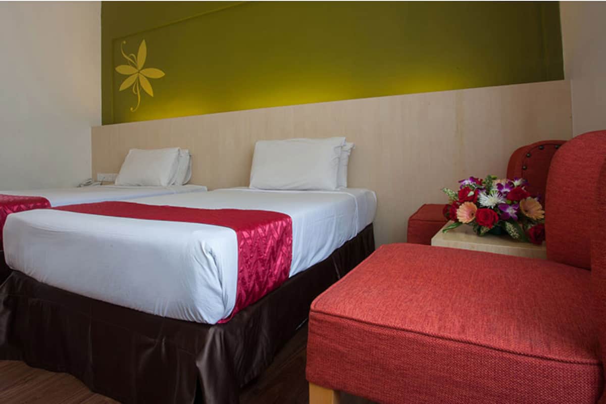 Une chambre d’hôtel avec deux lits, un fauteuil rouge et un arrangement floral.