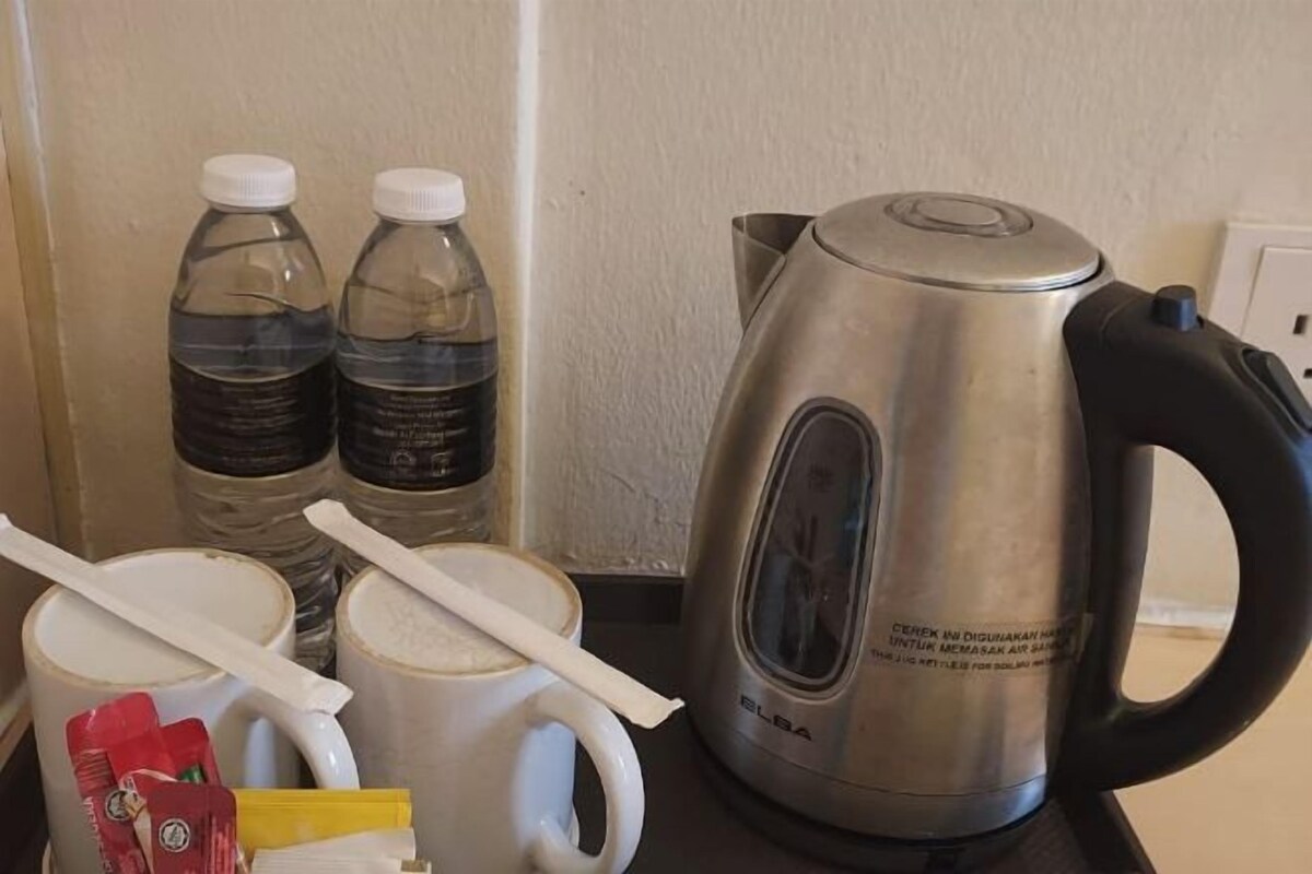 A kitchen counter with a stainless steel electric kettle, two water bottles, a white mug, and a white cup with a spoon.