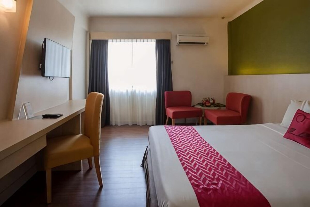 A hotel room with a bed, a desk, two chairs, a TV, and a window with curtains.