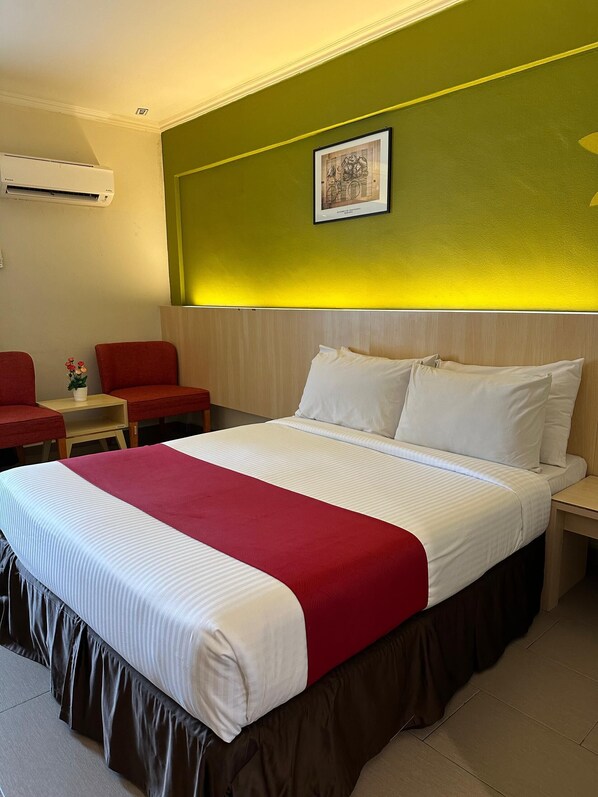 Habitación de hotel con una cama grande, ropa de cama roja y blanca, una pared de acento verde, un cuadro enmarcado y una silla roja.