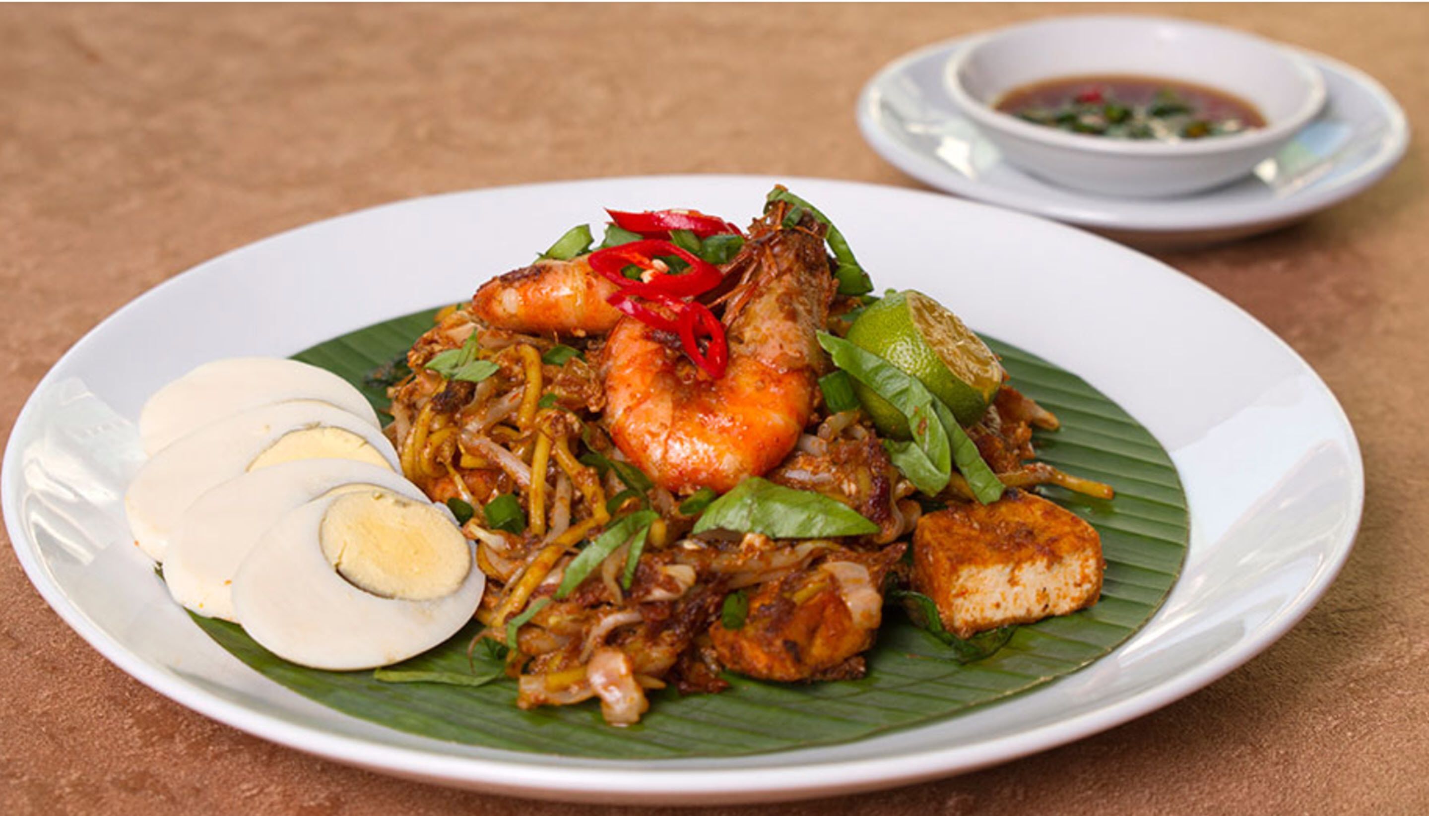 A plate of noodles with shrimp, vegetables, and a boiled egg on a banana leaf.