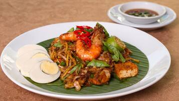 A plate of noodles with shrimp, vegetables, and a boiled egg on a banana leaf.