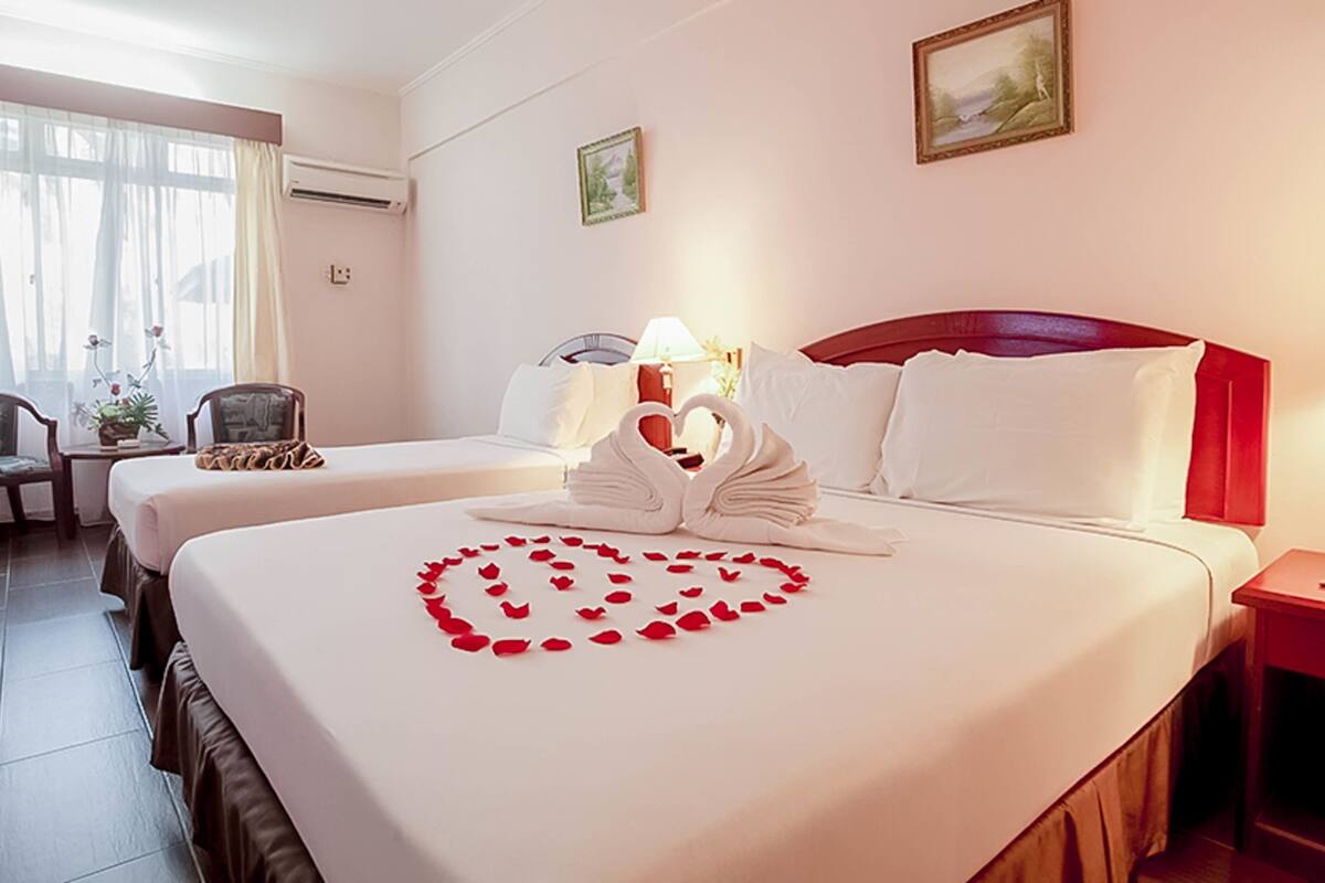 A hotel room with two beds, a sitting area with a chair and a table, and a view of the outdoors through the window.