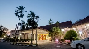 Ein Hotel mit Eingangsbereich, einer überdachten Laube, Palmen und einem weißen Auto davor.