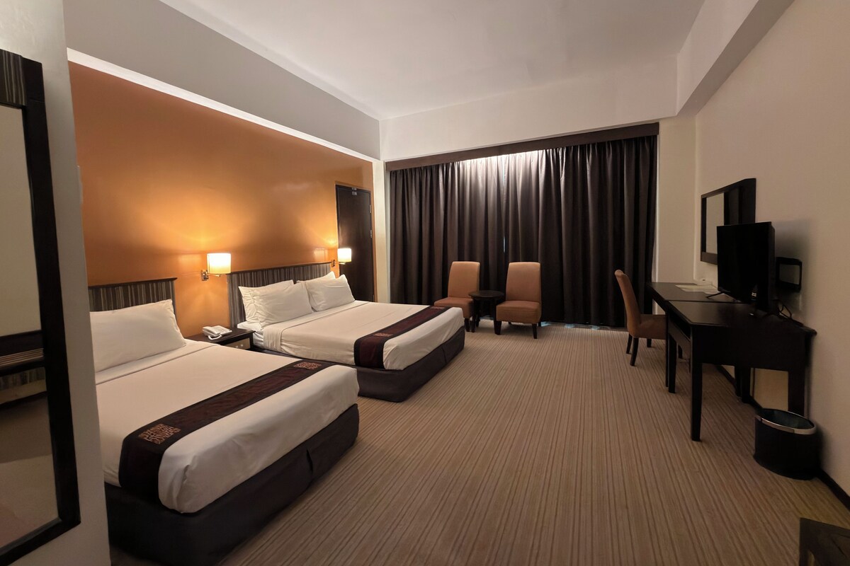 A hotel room with two beds, a desk, a chair, a television, and a large window with curtains.