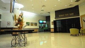 En modern entréhall med en receptionsdisk, en stor prydnadsväxt och en skylt med texten ”DEWAN SERI SARI”.