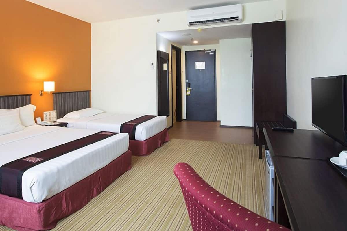 A hotel room with two beds, a desk, a TV, and an air conditioning unit.