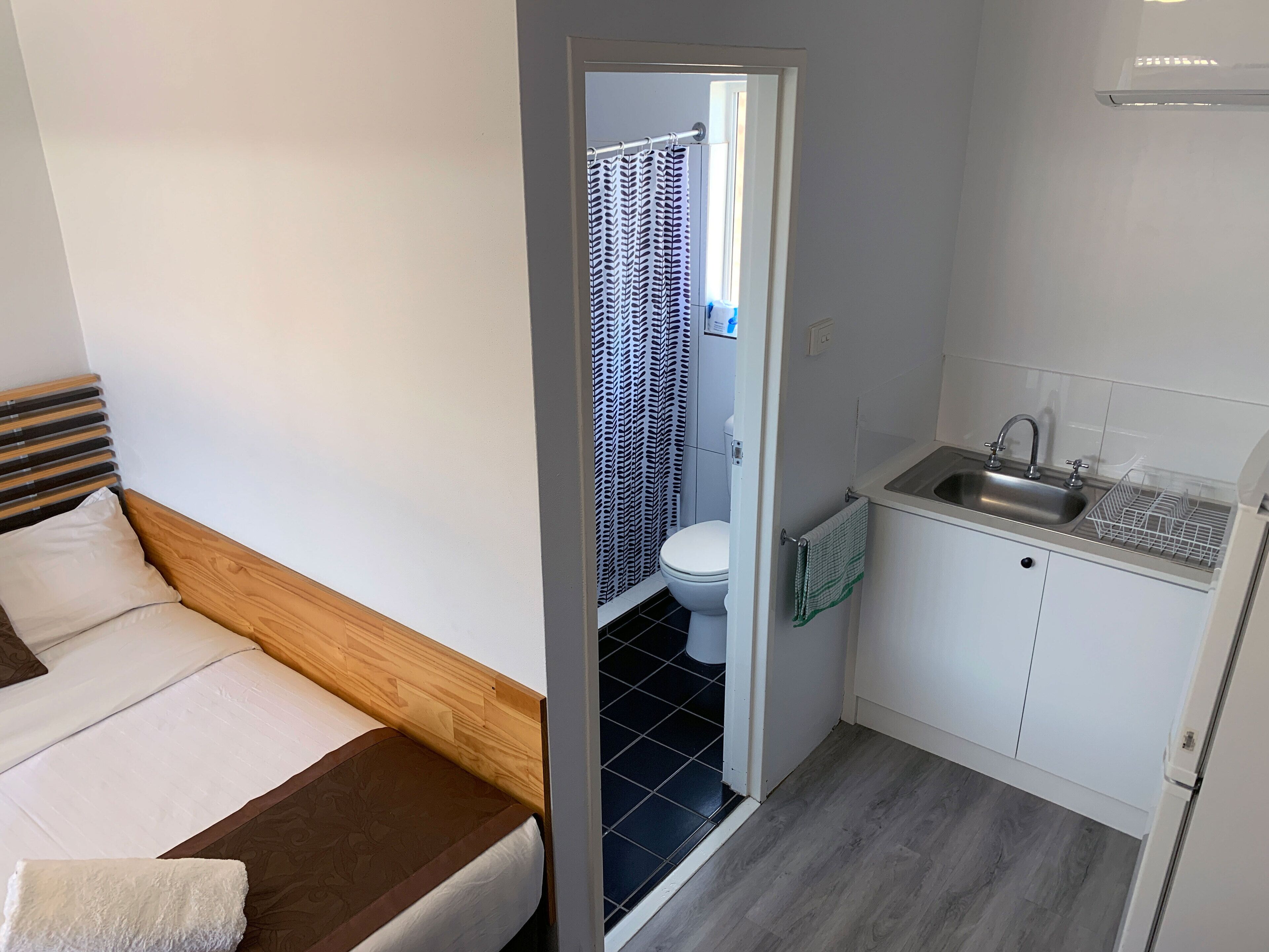 Et lille værelse med seng, et tekøkken og badeværelse med toilet og bruseforhæng.