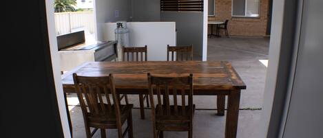 A dining area with a wooden table and chairs, a kitchen area with a refrigerator and stove, and a view of a brick building through the window.