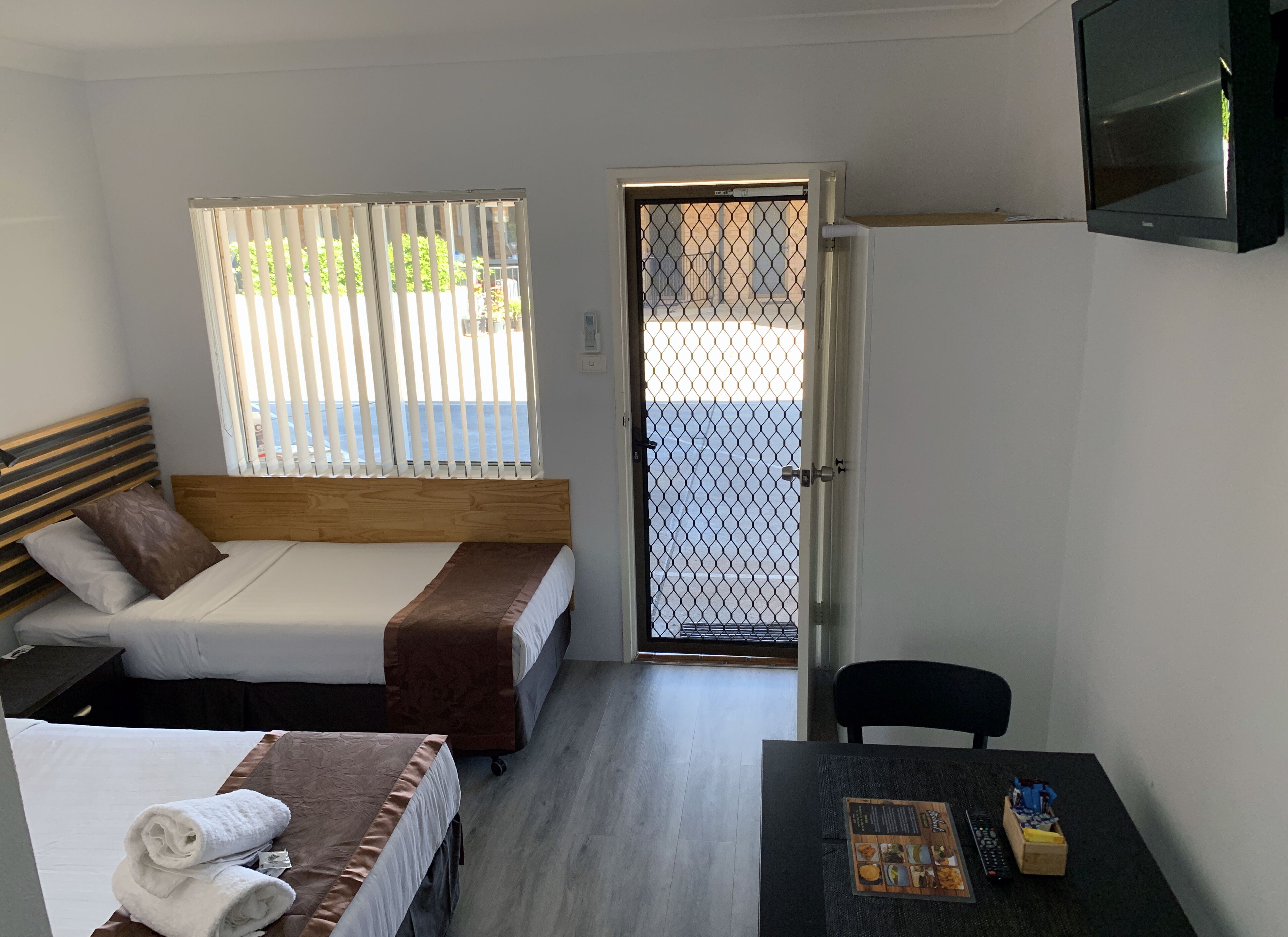 Habitación de hotel con dos camas, un televisor, una mesa con un menú y vistas a través de una puerta.