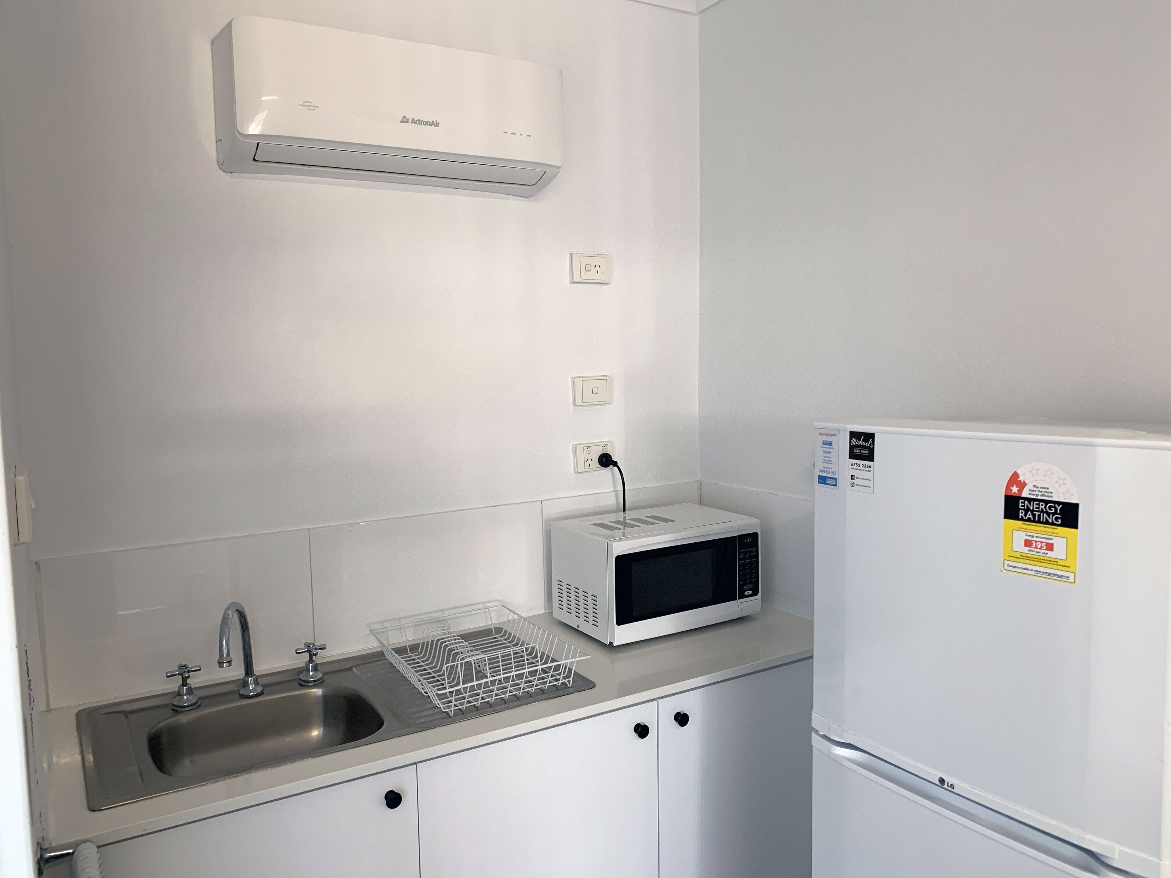 A kitchenette with a white refrigerator, a microwave, a sink, and an air conditioner.