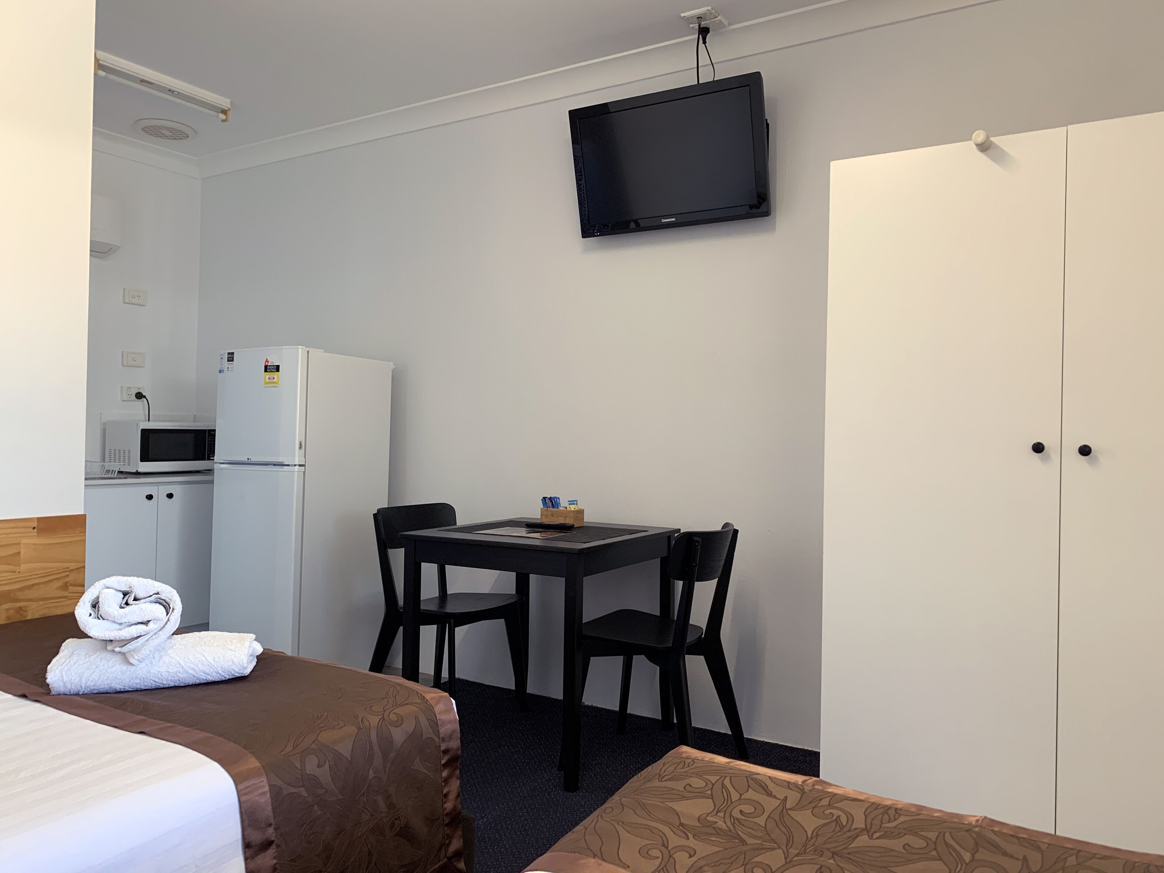 A hotel room with a bed, a desk with two chairs, a television, a microwave, and a refrigerator.