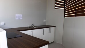 A compact kitchen with a dark wooden countertop, white cabinets, and a stainless steel sink. A sign with kitchen rules is visible on the wall. - Baths Motel (Moree)
