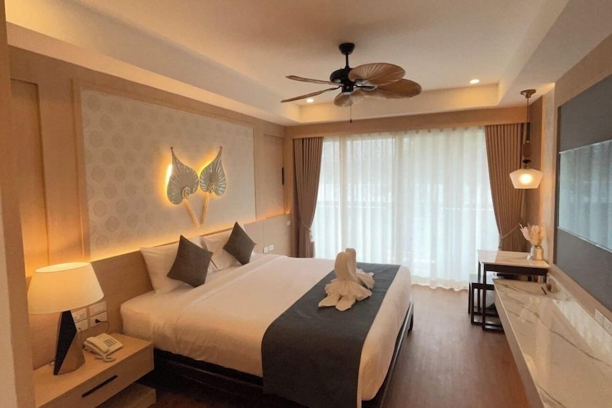A hotel room with a bed, bedside table, lamp, and a ceiling fan.