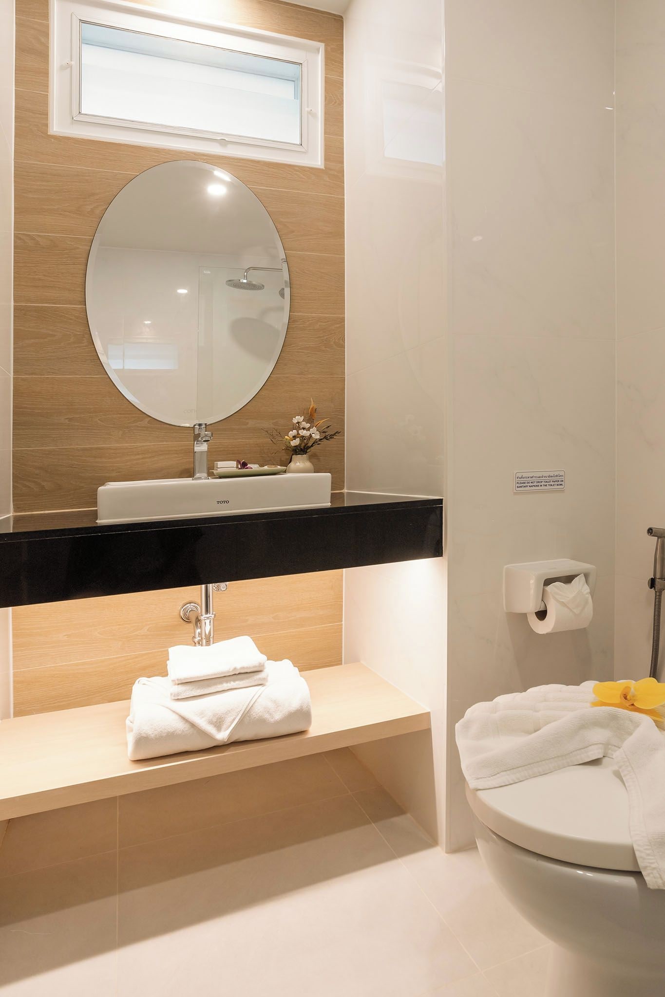 A modern bathroom with a round mirror, a black countertop, a white sink, a toilet, and a towel rack.