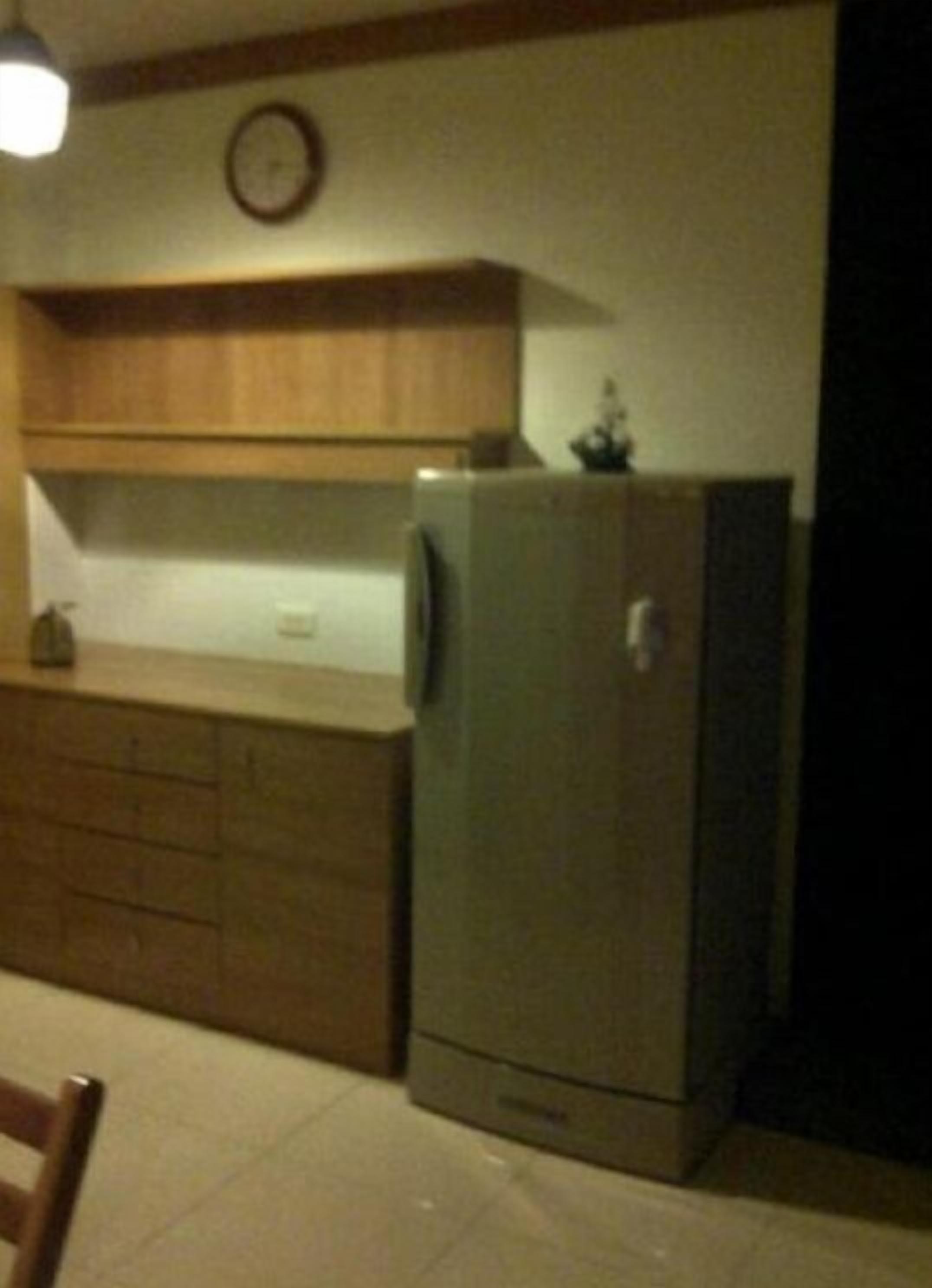 Een keuken met houten kastjes, een koelkast en een klok aan de muur.