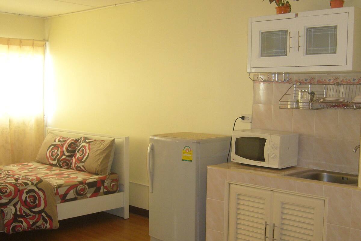 Una habitación compacta con cama, refrigerador, microondas y una pequeña zona de kitchenette.