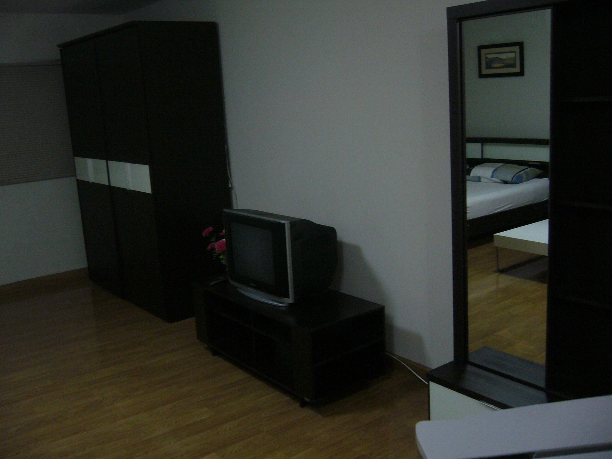 Una habitación con una cama, un televisor sobre un mueble bajo, un armario y un espejo que refleja la cama.