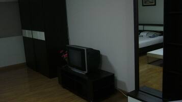Una habitación con una cama, un televisor sobre un mueble bajo, un armario y un espejo que refleja la cama.