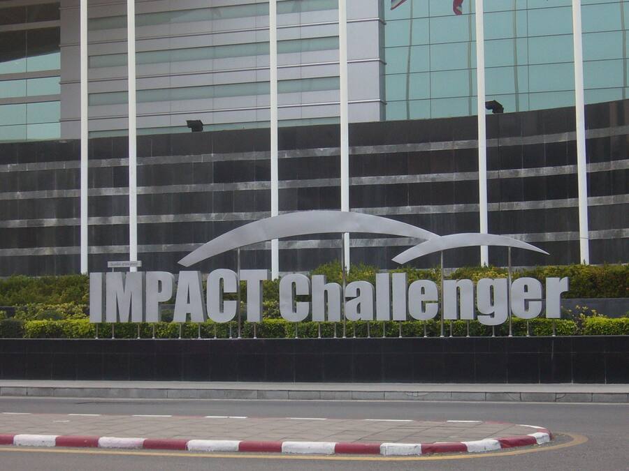 Un cartel con la inscripción 'IMPACT Challenger' frente a un edificio moderno con ventanas reflectantes.