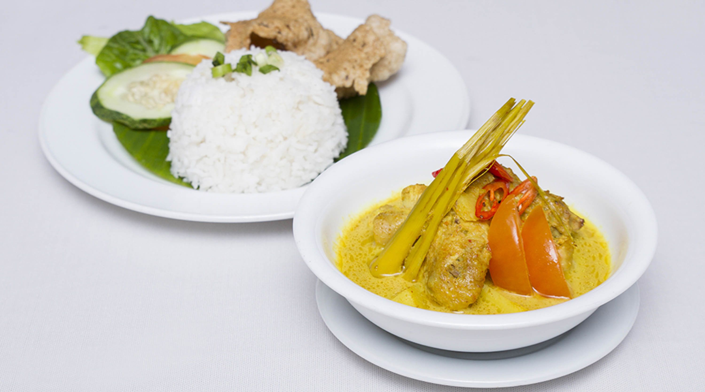 A plate with white rice, cucumber slices, fried items, and a bowl of yellow curry with vegetables.