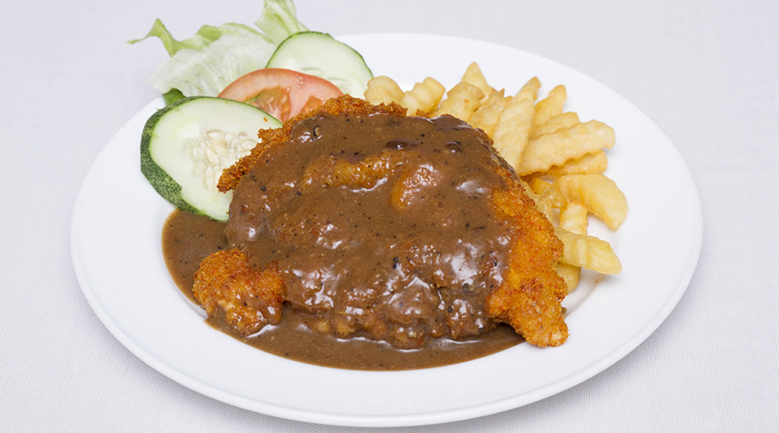 A plate with a breaded and fried cutlet topped with brown sauce, accompanied by French fries and a side salad of lettuce, tomato, and cucumber.