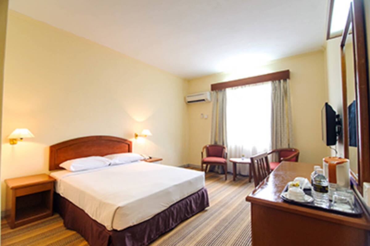 A hotel room with a bed, bedside tables, a desk with a chair, a television, and a window with curtains.