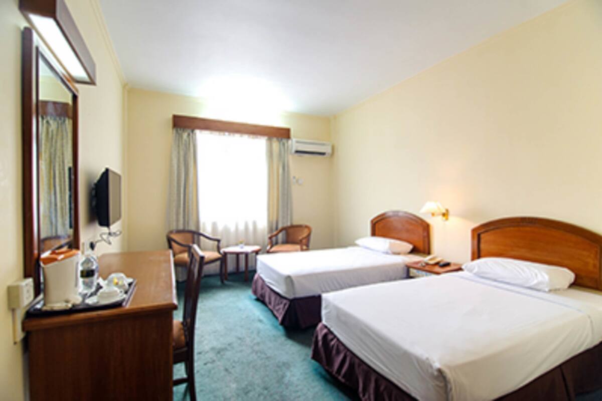 A hotel room with two beds, a desk with a chair, a small table, and a mirror.
