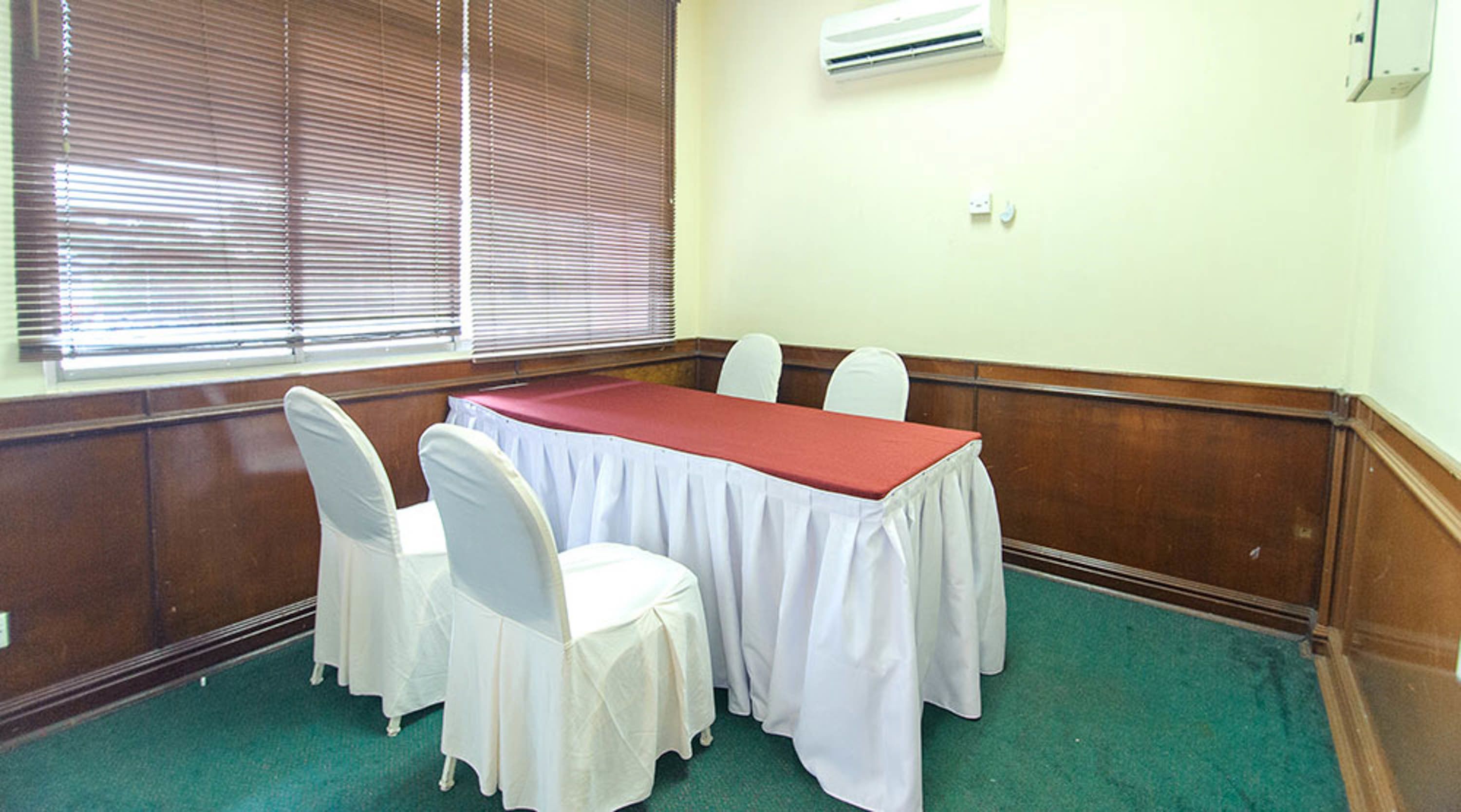 A conference room with a long table, white chairs, and a red tablecloth.