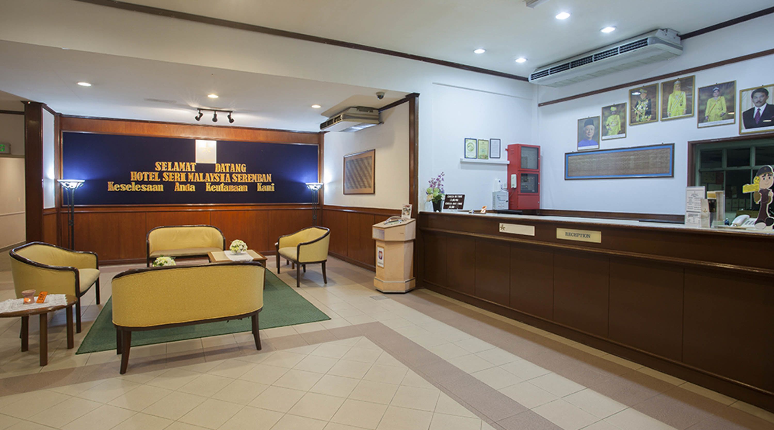 A hotel reception area with a reception desk, chairs, and a wall with framed pictures.