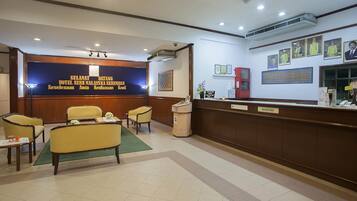 A hotel reception area with a reception desk, chairs, and a wall with framed pictures.