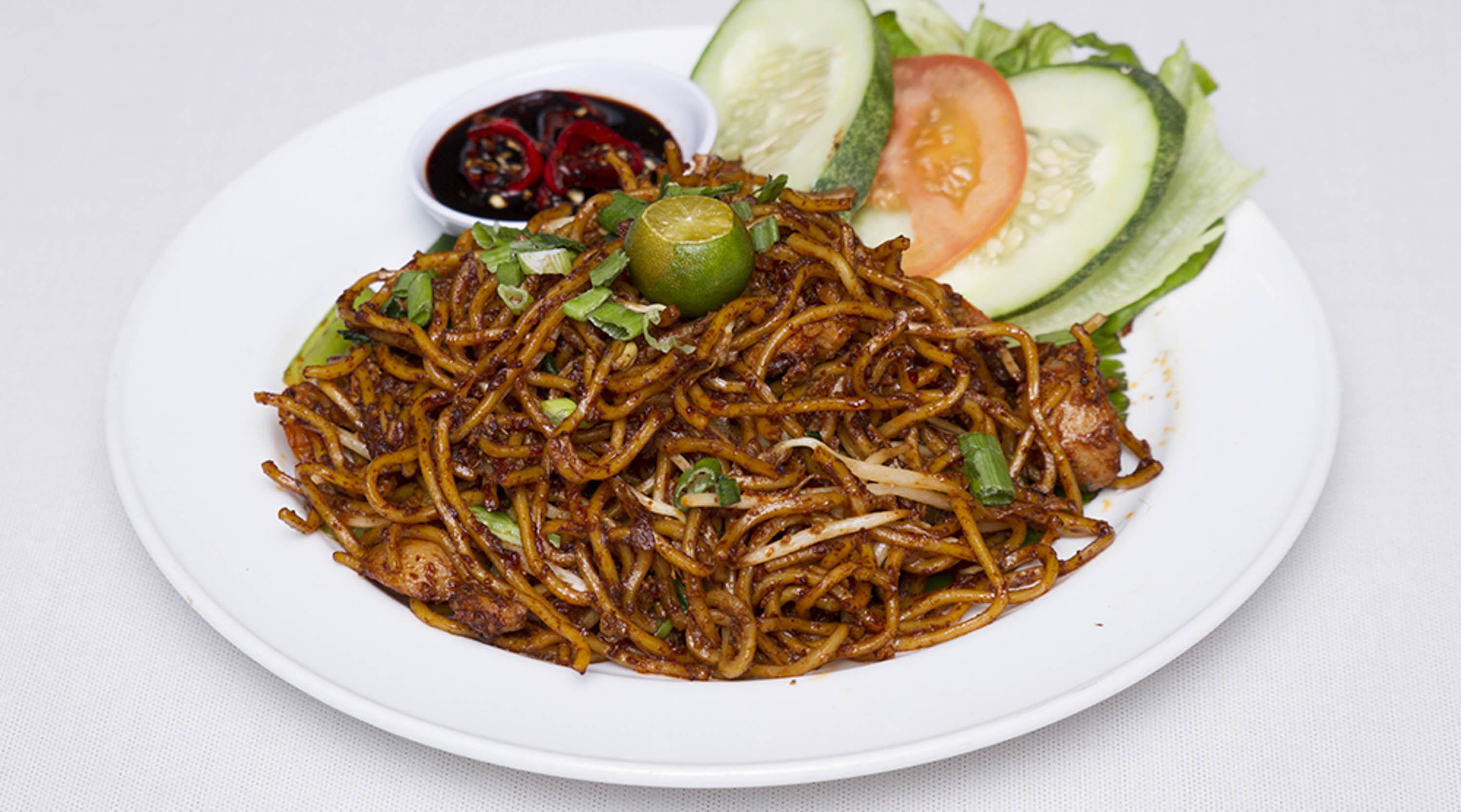 Un plato de fideos salteados con vegetales y una salsa para mojar.