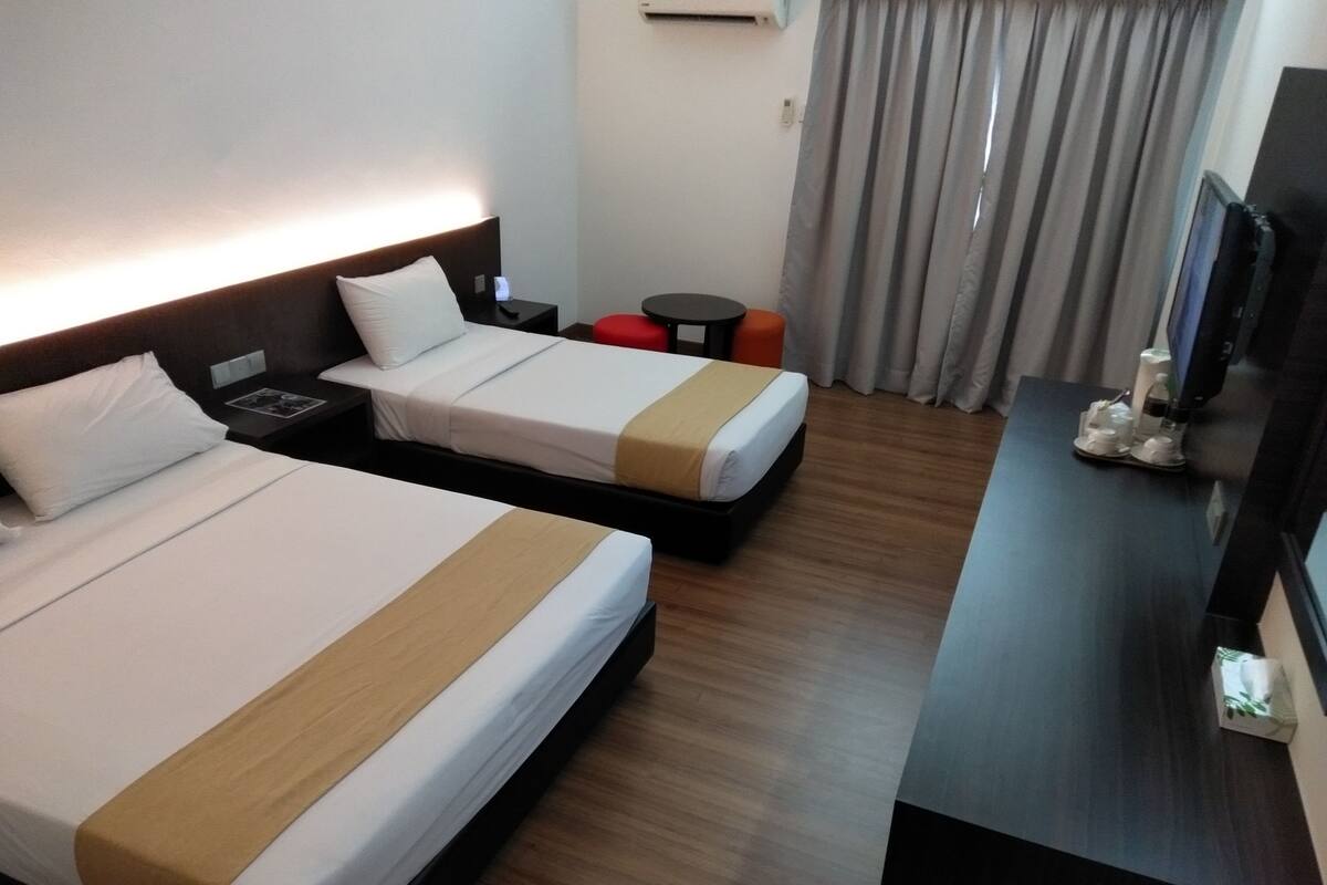 A hotel room with two beds, a desk, a chair, a TV, and a window with curtains.