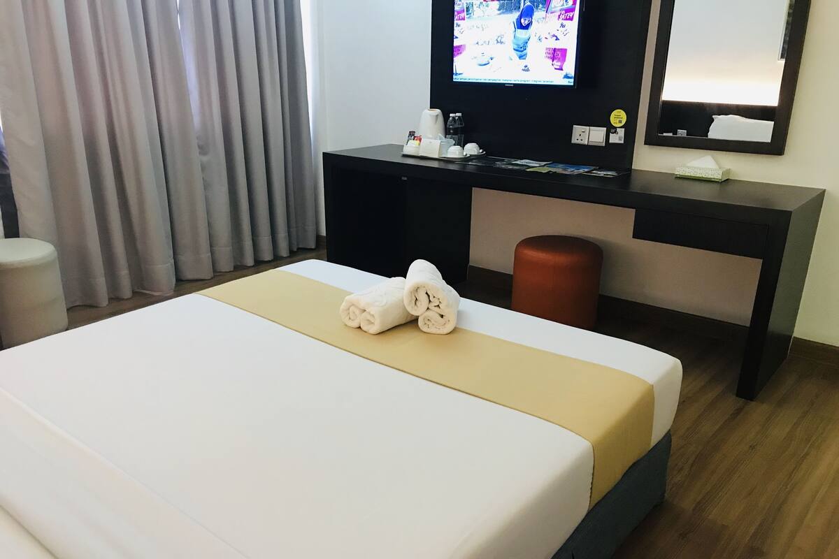 A hotel room with a bed, a desk, a television, and a mirror.