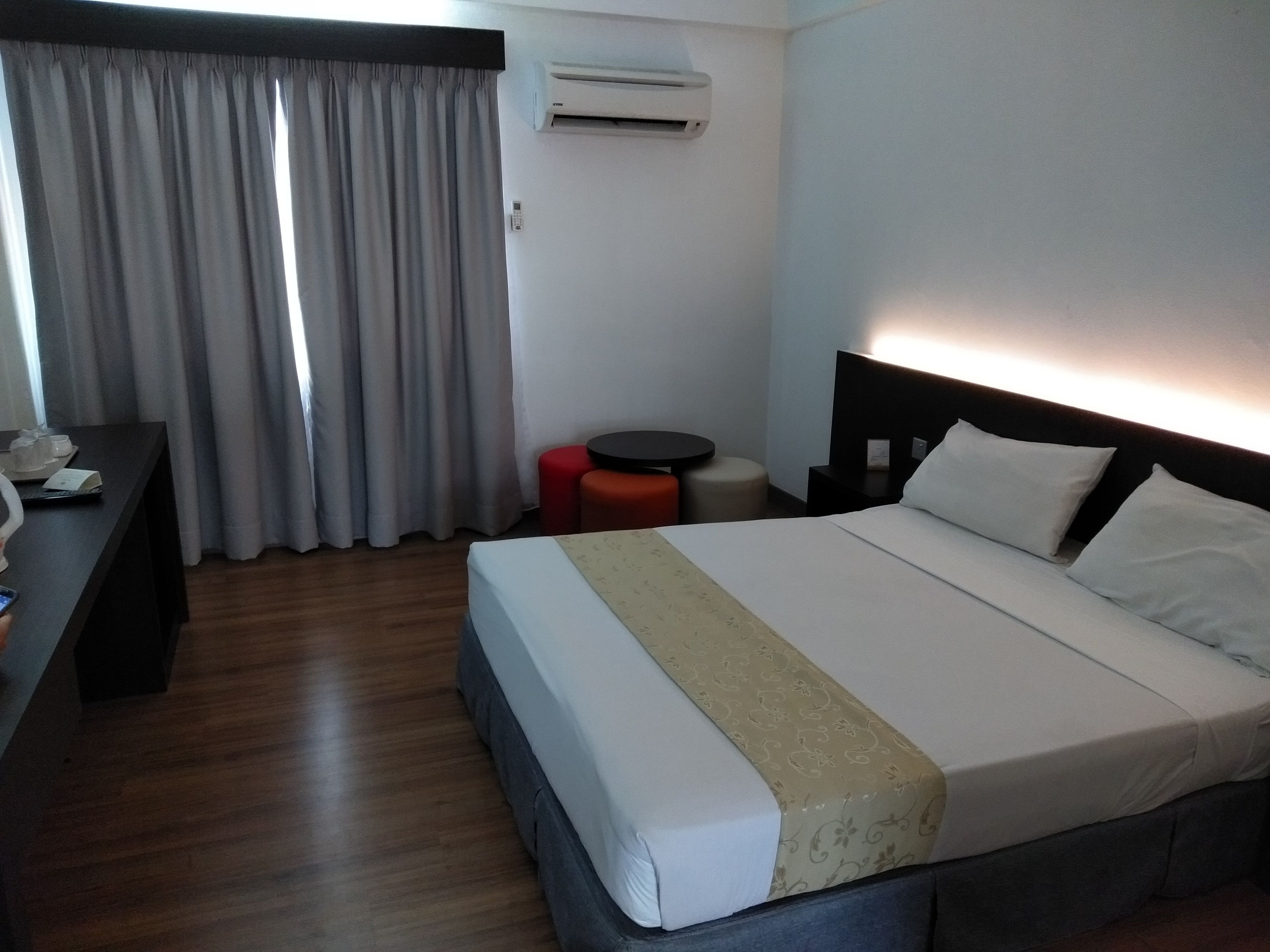 Habitación de hotel con cama, escritorio, silla, mesita y ventana con cortinas.