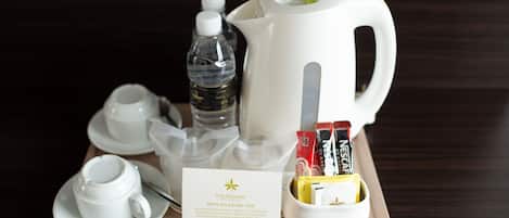 A tray with a white coffee pot, a water bottle, a cup, a saucer, a tray of coffee packets, and a card with hotel information.
