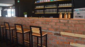 A bar area with brick walls, wooden bar stools, shelves with glassware, and a sign with the name 'Rasa Rasa SG Petoni'.