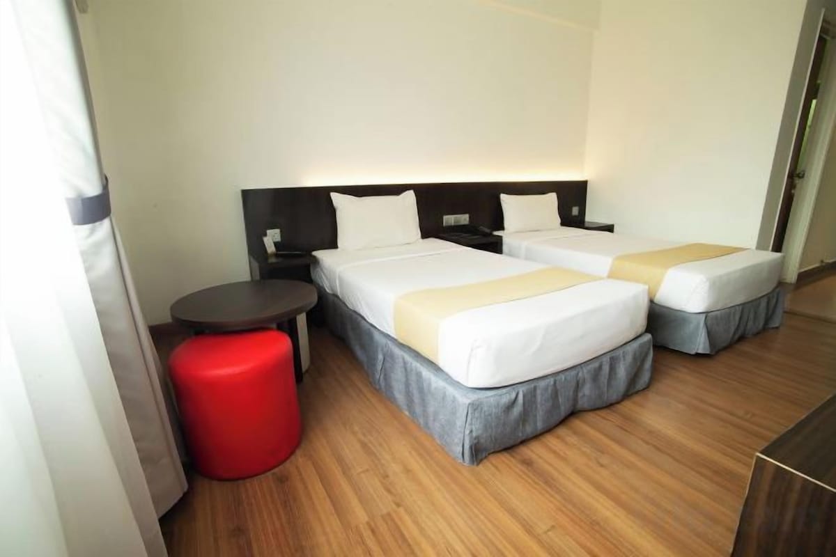 A hotel room with two beds, a small round table, and a red stool.