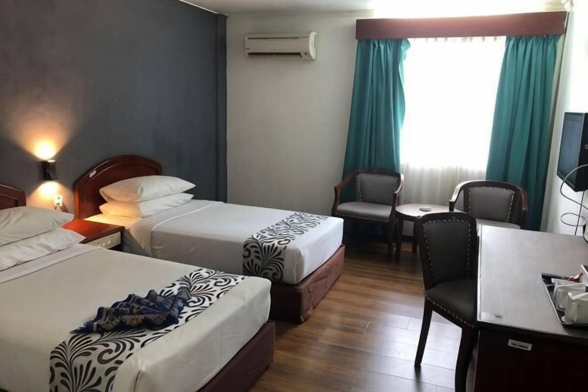 A hotel room with two beds, a desk, a chair, and a TV.