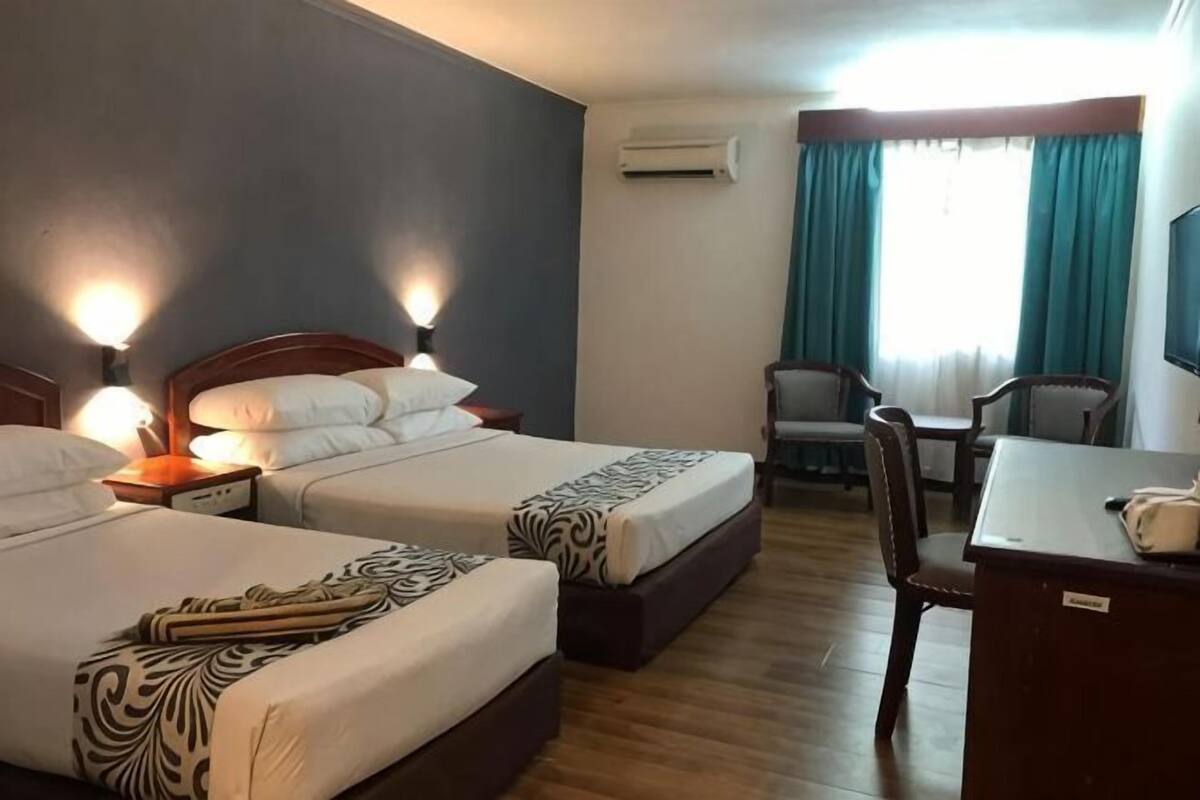 A hotel room with two beds, a desk, a chair, and a TV.