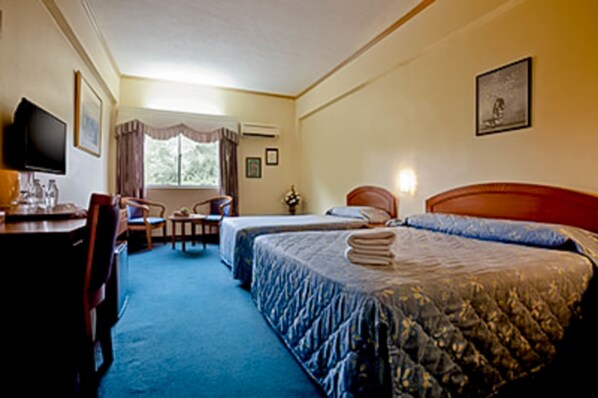 A hotel room with two beds, a desk with a chair, a television, and a window with curtains.