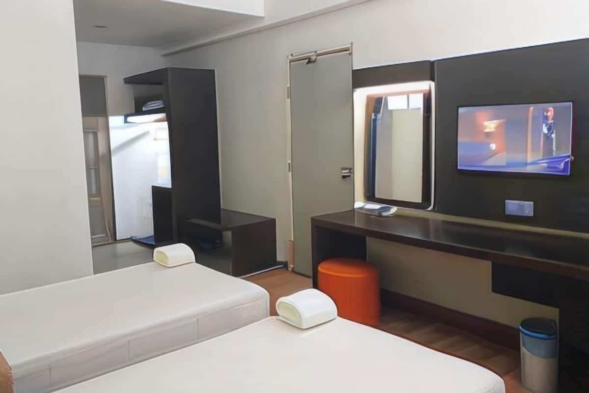 A modern hotel room with a bed, a mirror, a television, and a small orange stool.