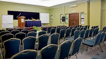 Un salón de conferencias con filas de sillas azules, un atril, una pizarra y una puerta con la etiqueta 'KELUAR'.