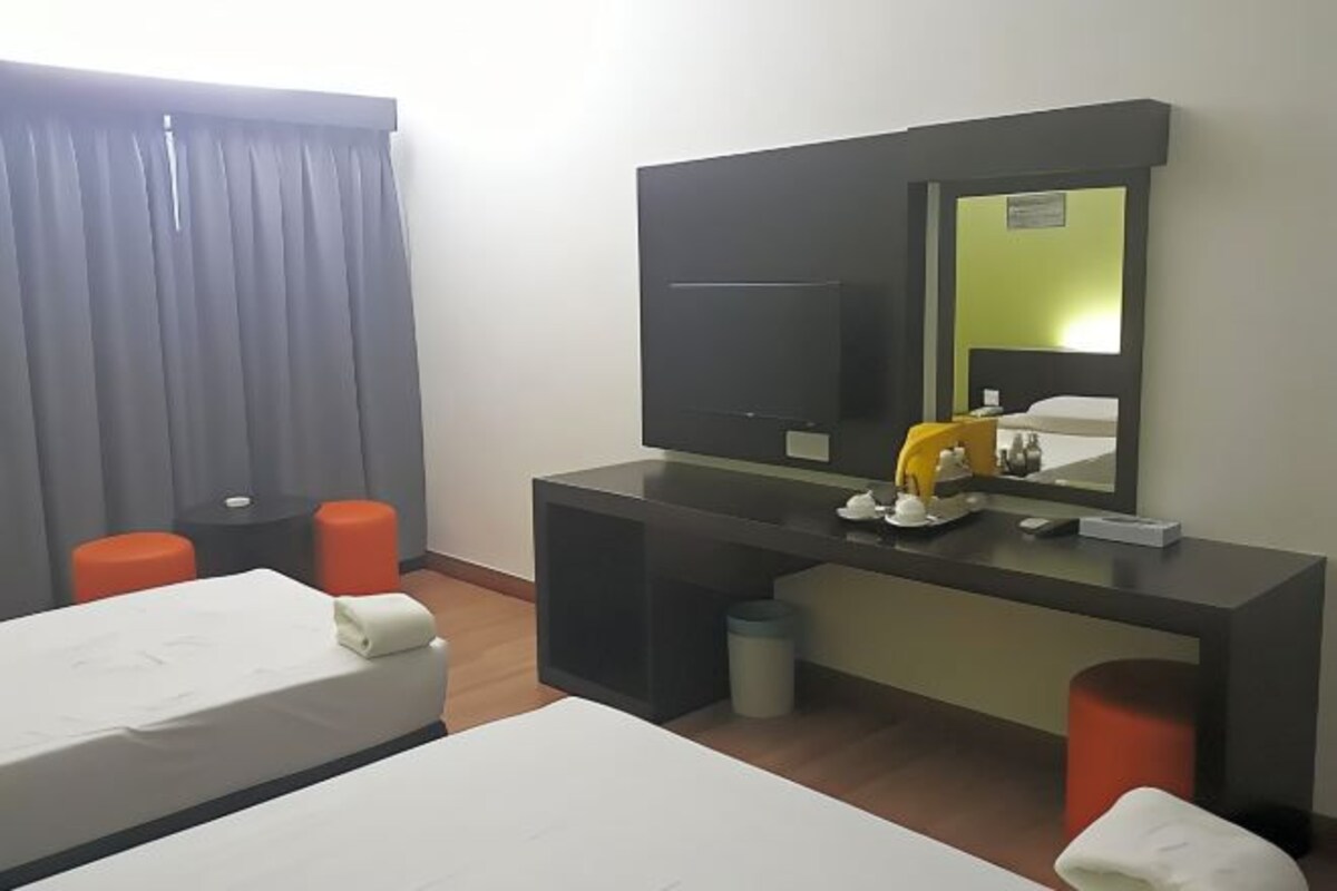 A hotel room with two beds, a desk with a mirror, a television, and orange stools.