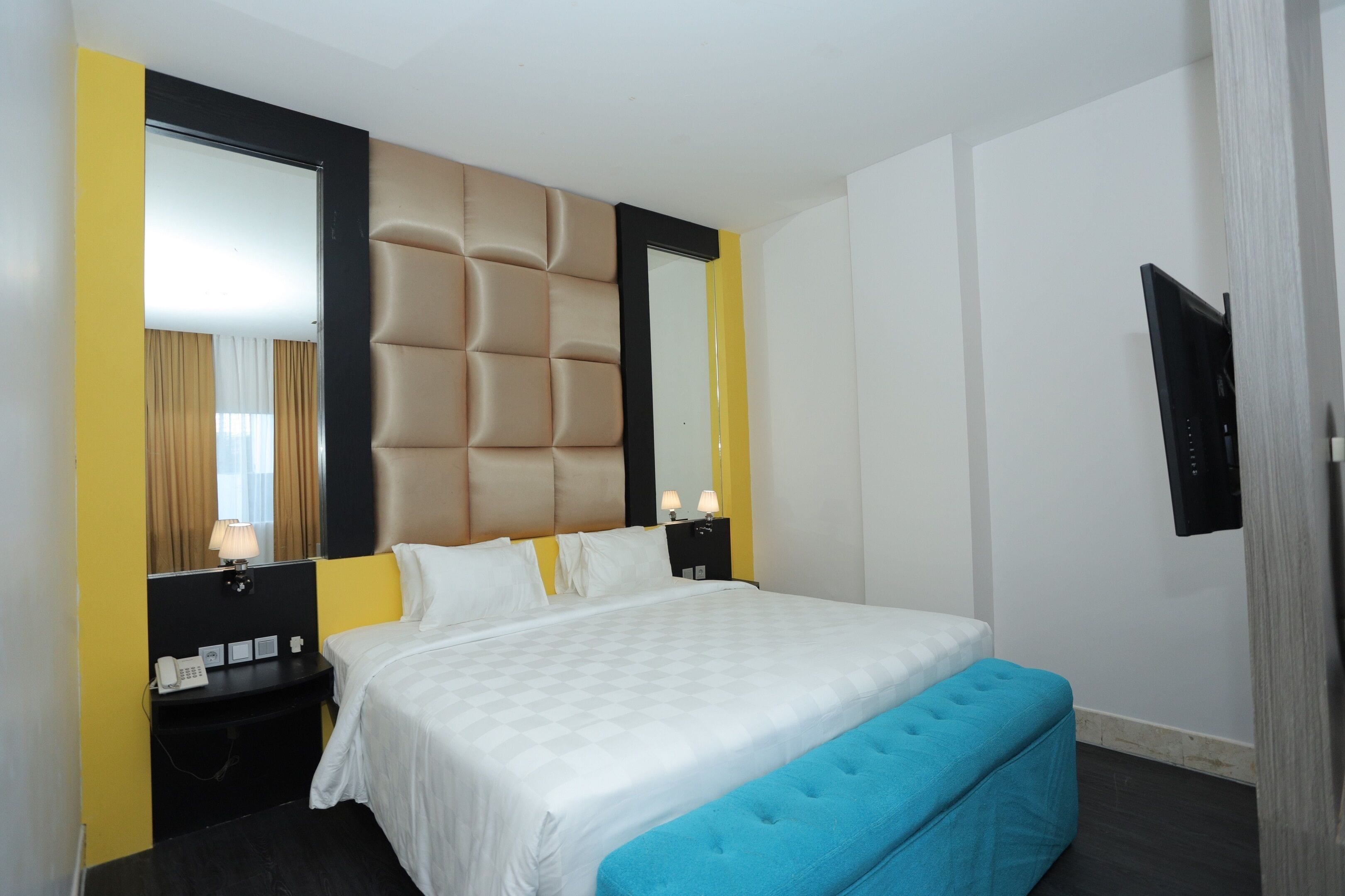 A hotel room with a large bed, a bedside table with a lamp, a mirror, and a TV mounted on the wall.