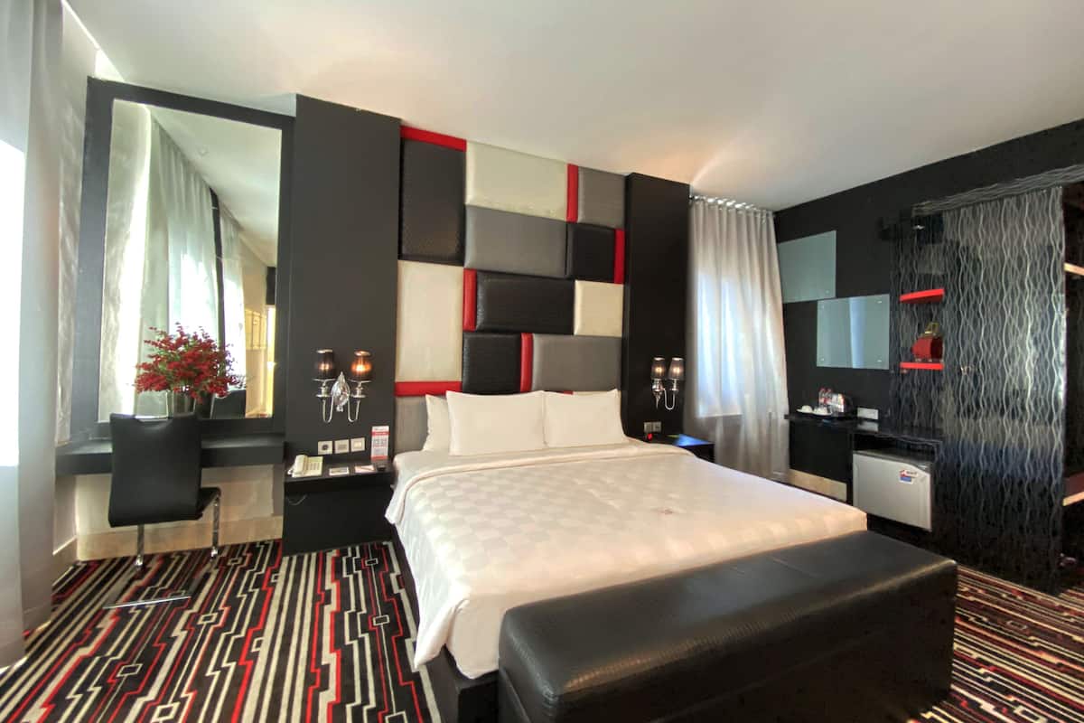 Una habitación de hotel moderna con una cama grande, un escritorio, una silla, una mesita, un espejo y una alfombra estampada.